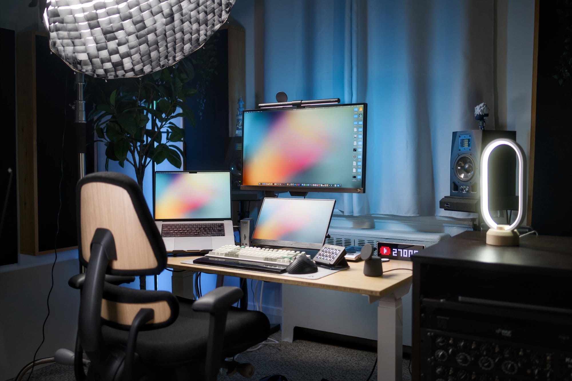 A desk setup featuring an Anthros Chair, a BenQ EW2780U monitor with a Quintis ScreenLinear Light Bar, an M1 Max MacBook Pro, a Keychron Q12 Max keyboard, and a ProtoArc EM01 trackball mouse