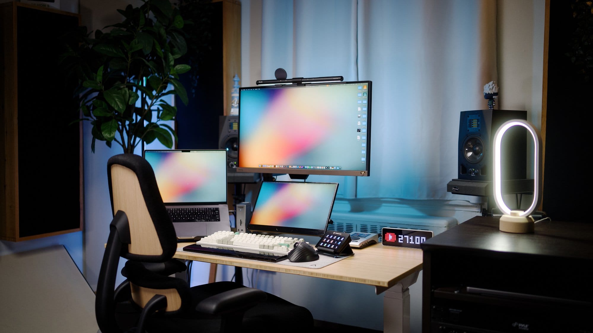 A desk setup with an Anthros Chair, a BenQ EW2780U monitor with a Quintis ScreenLinear Light Bar, an M1 Max MacBook Pro, and a Keychron Q12 Max keyboard