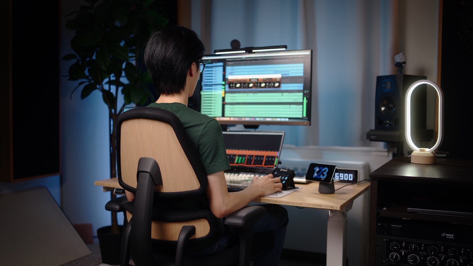 A person sitting on an Anthros Chair at a desk, using a BenQ EW2780U monitor with a Quintis ScreenLinear Light Bar, an M1 Max MacBook Pro, and a Stream Deck Classic