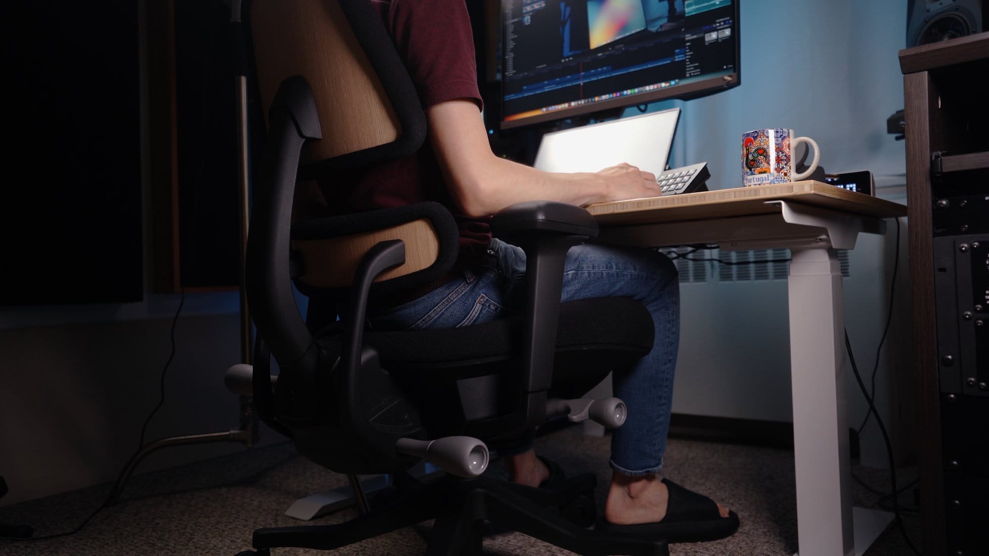 A close-up of a person sitting on an Anthros Chair at a Flexispot standing desk