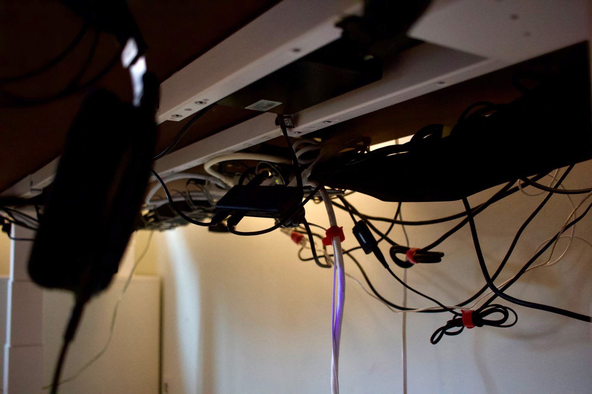 A view under a desk showing cable management with power strips, adapters, and cords secured using cable ties and clips