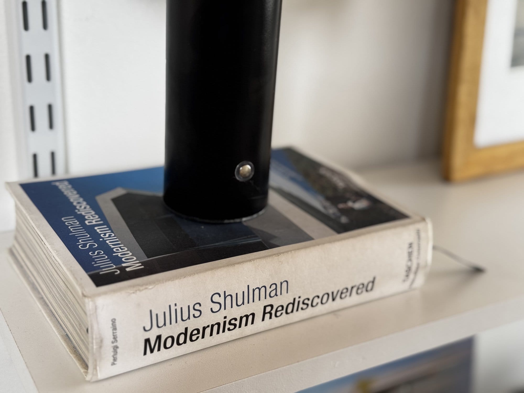 A close-up of the book Modernism Rediscovered by Julius Shulman on a white shelf