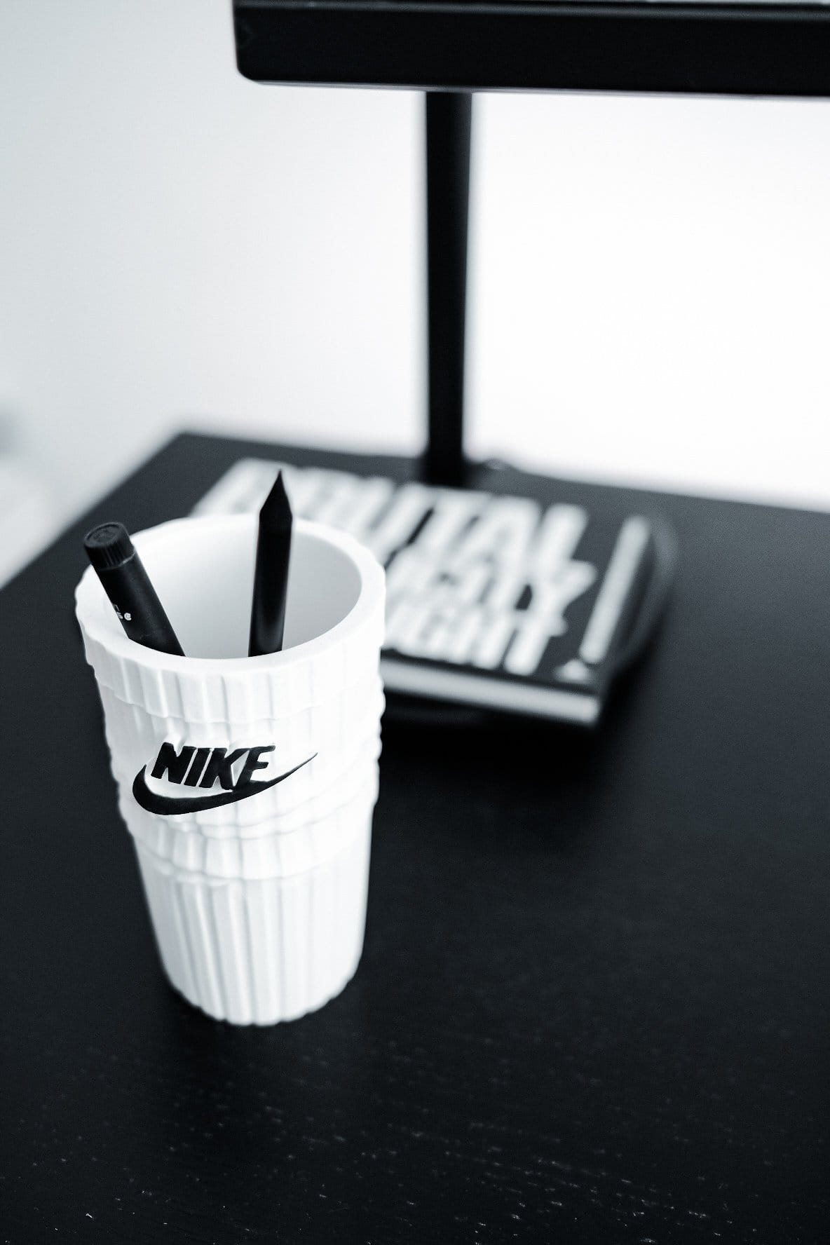 A white Nike cup holding two black pens on a black desk