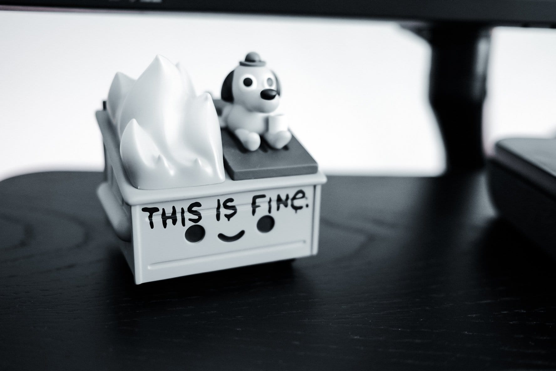 A “This Is Fine“ vinyl figurine with a smiling box, flames, and a small dog sitting on top