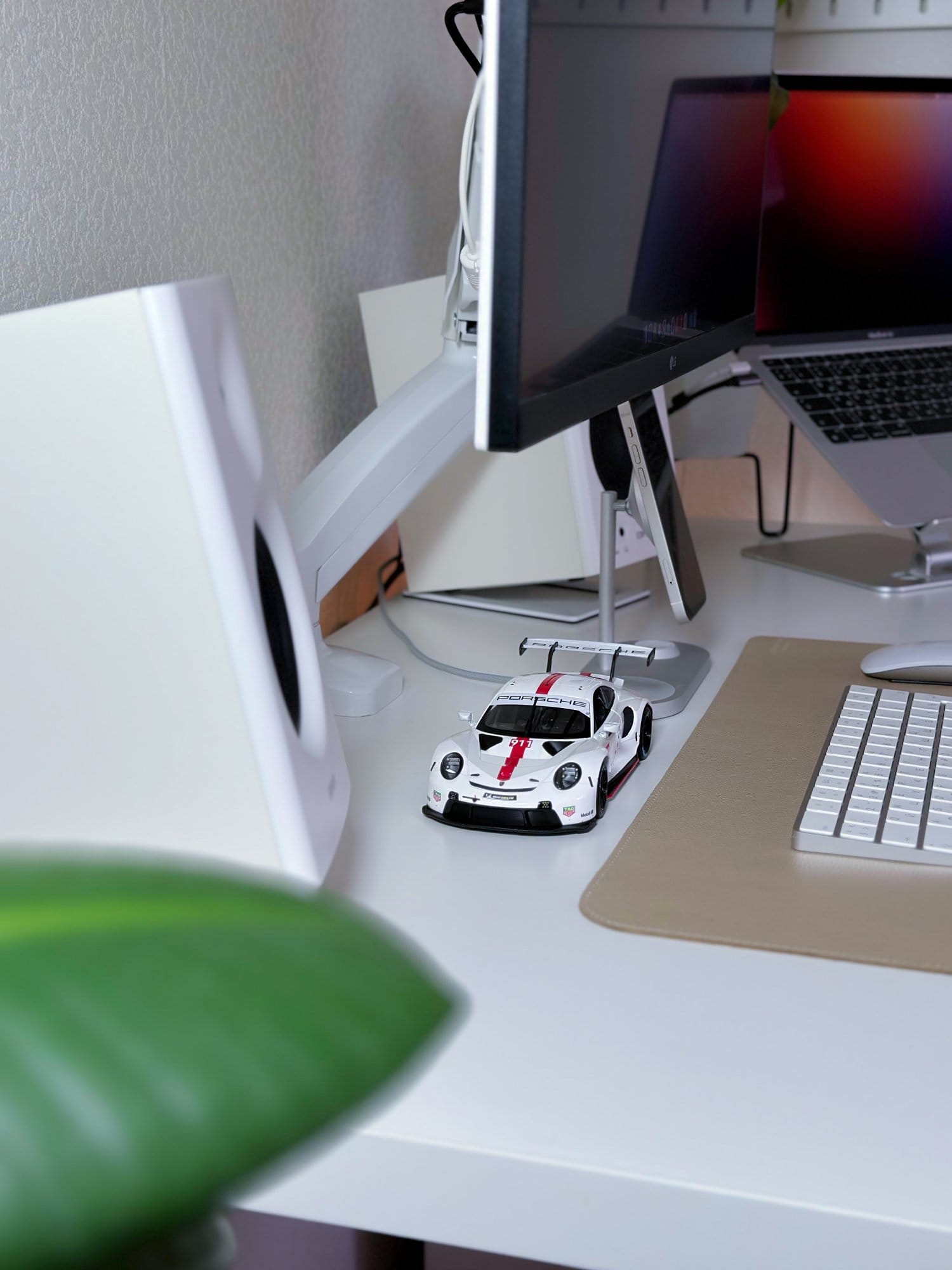 A close-up of a workspace with an LG 27UL650-W monitor on an ONKRON G80 mount, Edifier MR4 speakers, a MacBook Air M1 2020, and a Porsche model car on the desk