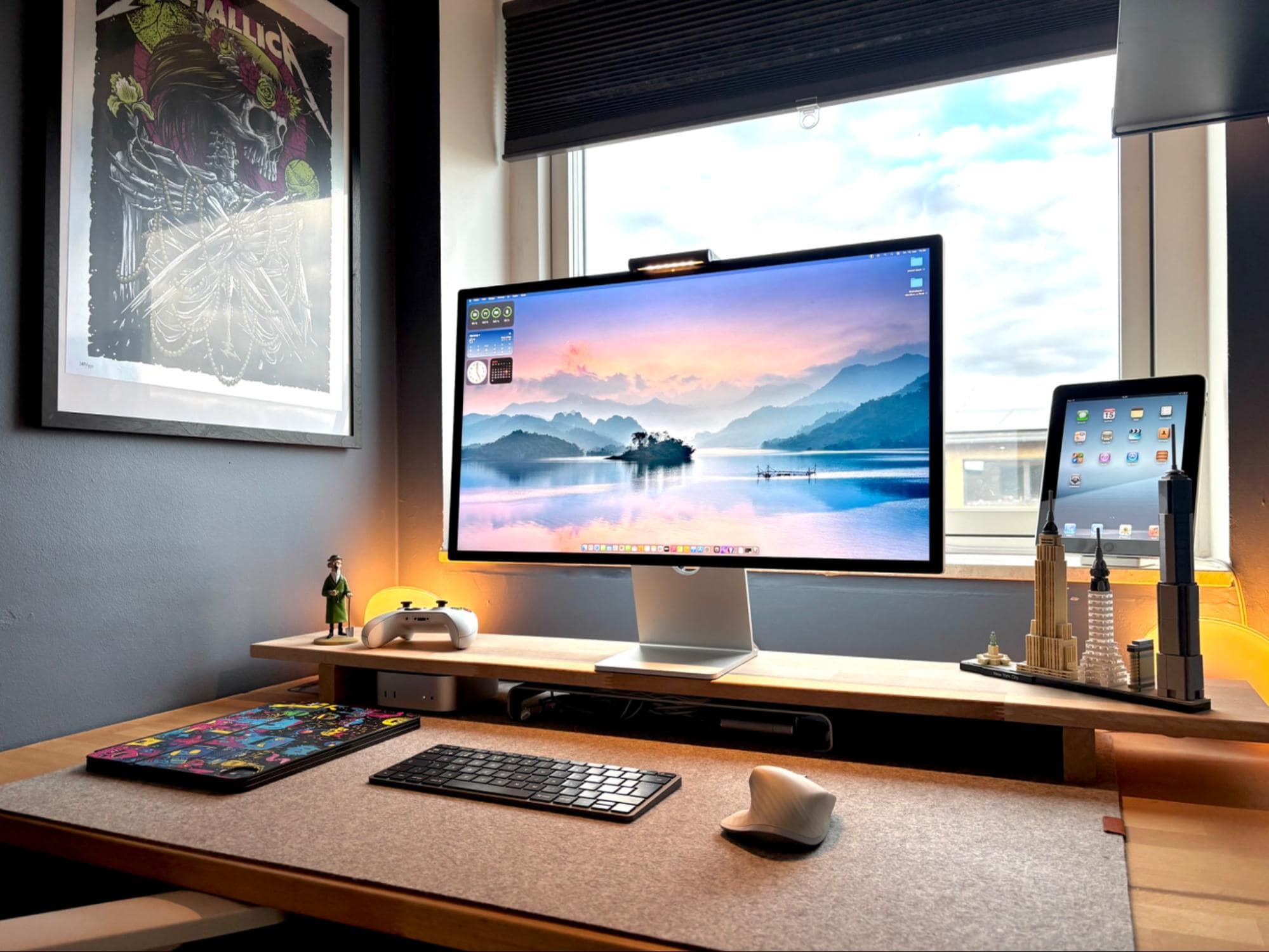 A home office setup with an Apple Studio Display, Mac Mini M4, Logitech MX Master for Mac mouse, and a closed iPad Pro M4 13″ on a felt desk mat, with an older iPad resting on a stand