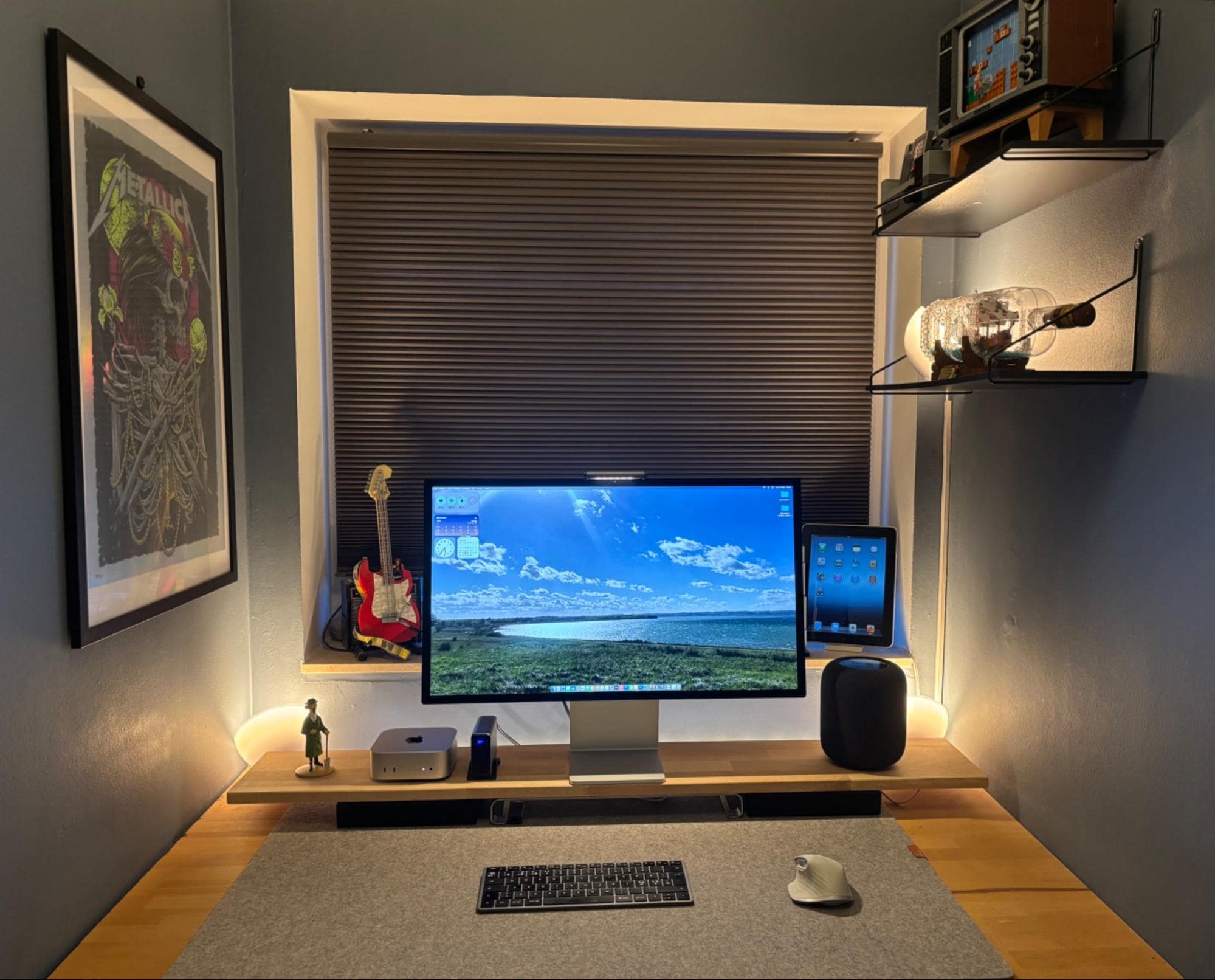 A small home office setup with an Apple Studio Display, Mac Mini M4, Apple HomePod 2nd Gen, iPad, Logitech MX Master for Mac mouse, and a Satechi keyboard on a felt desk mat