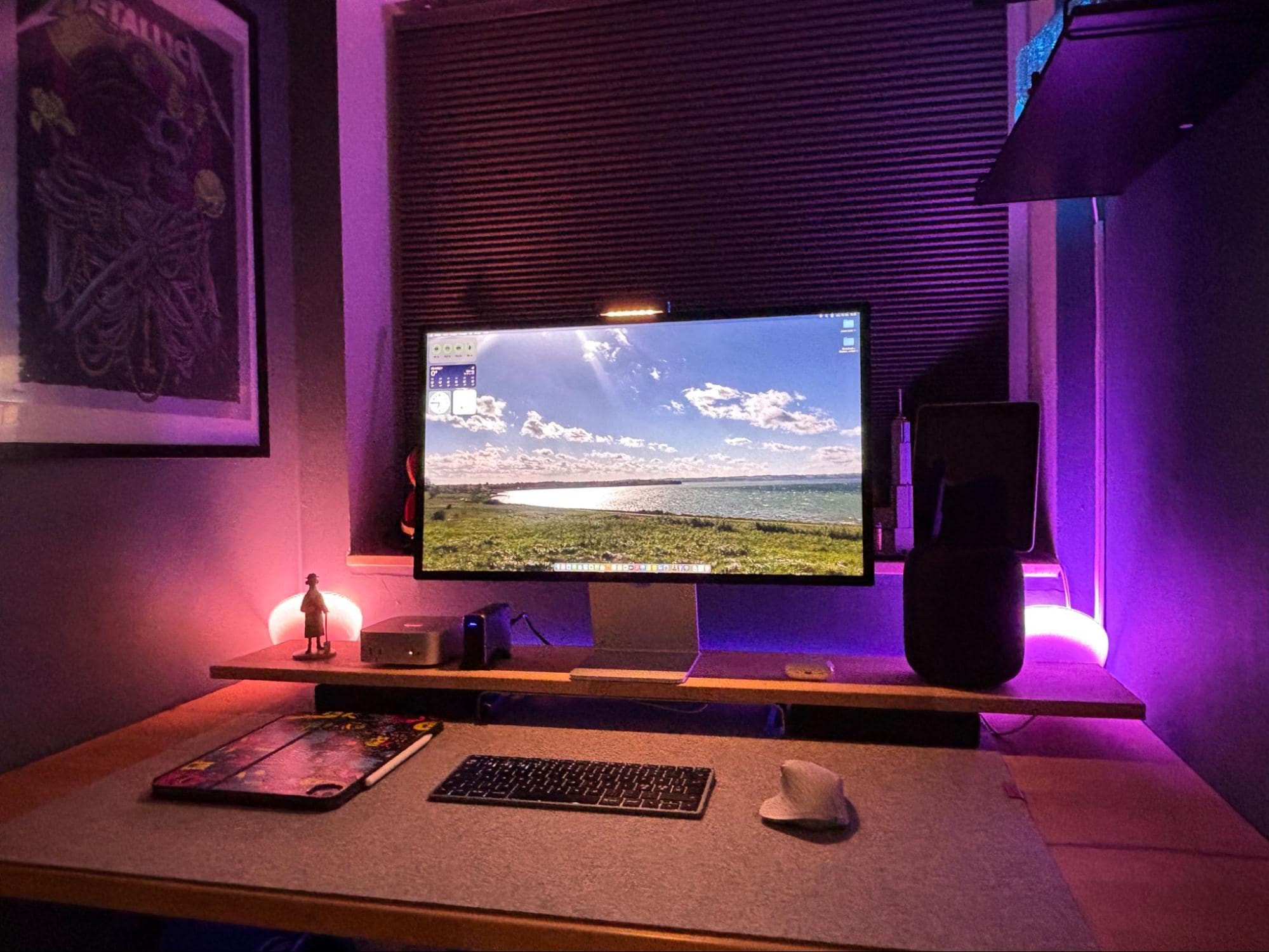 A desk setup with an Apple Studio Display, Mac Mini M4, Satechi keyboard, Logitech MX Master for Mac mouse, Apple HomePod 2nd Gen, and a closed iPad Pro M4 13″ on a felt desk mat under purple ambient lighting