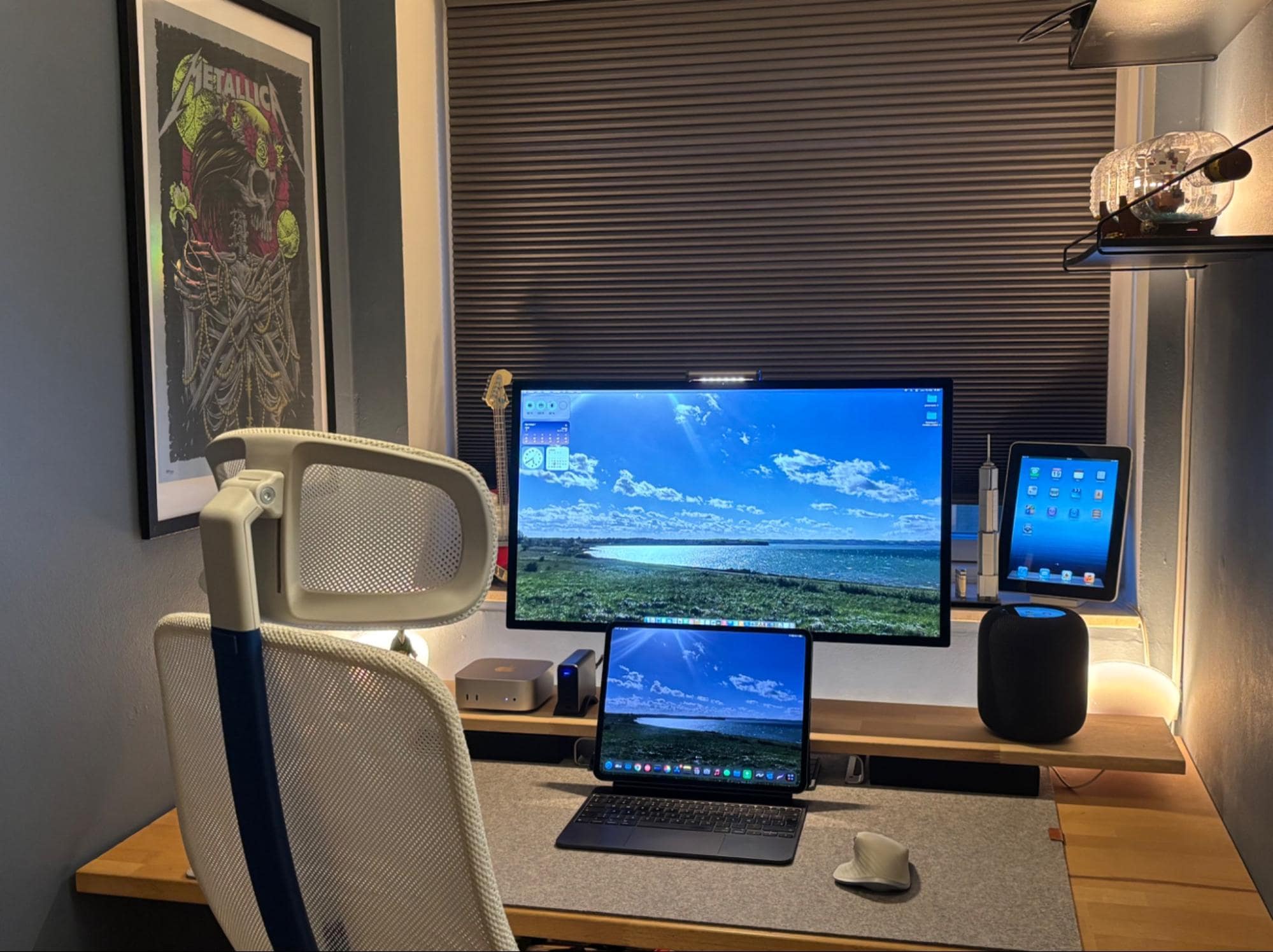 A workspace setup with an Apple Studio Display, Mac Mini M4, MacBook Air M1, Logitech MX Master for Mac mouse, and an Apple HomePod 2nd Gen on a desk shelf