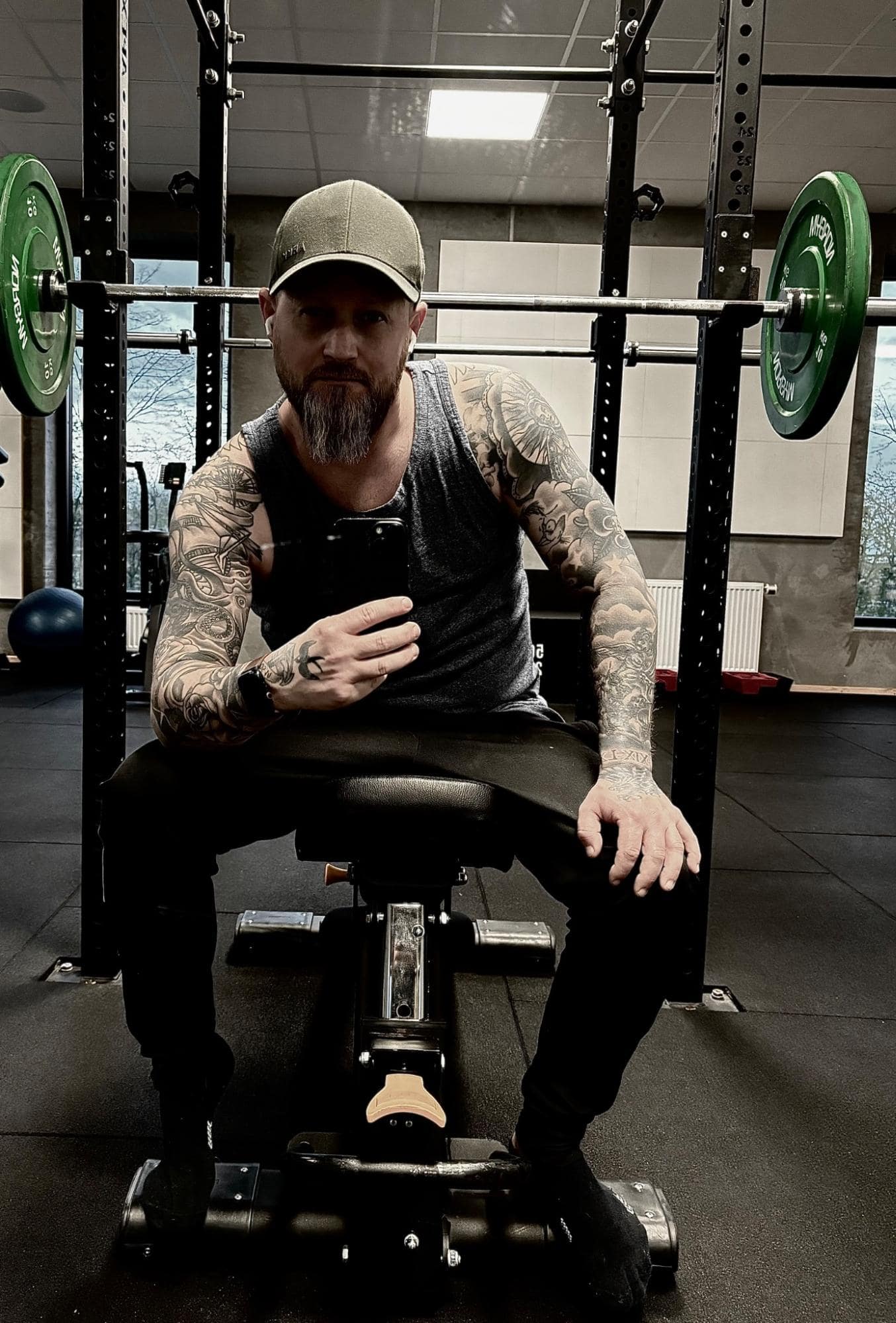 Nicolai Jul, the owner of the small Apple desk setup, with tattooed arms, a grey tank top, and a cap, taking a mirror selfie in a gym